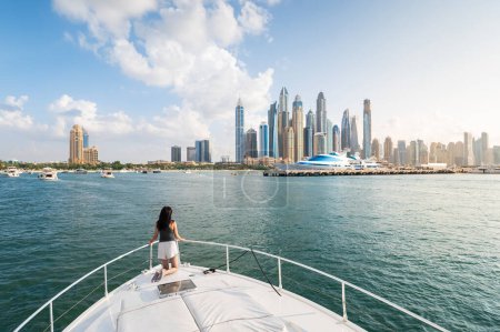 Bezaubernde Schönheit der Dubai Marina, als eine stilvolle Frau den ruhigen Sonnenuntergang während einer luxuriösen Jachtfahrt umarmt. Die Essenz von Raffinesse und Entspannung vor dem ikonischen Stadtbild Dubais in den Vereinigten Arabischen Emiraten