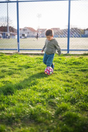 Capturé en milieu de jeu, ce tout-petit garçon se concentre sur le ballon de football, illustrant les fiançailles d'un enfant de 3 ans avec le football sur herbe. Une scène vibrante capture le jeu joyeux d'un petit garçon alors qu'il se promène autour d'un ballon de football sur l'herbe verte luxuriante.