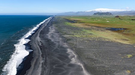 Langer schwarzer Strand vom Vorgebirge Dyrholaey aus mit dem Vulkan Eyafjiallajokull im Hintergrund