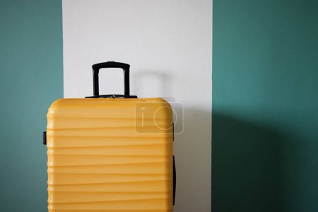 Photo for New yellow suitcase against the wall. Travel and vacation concept. - Royalty Free Image