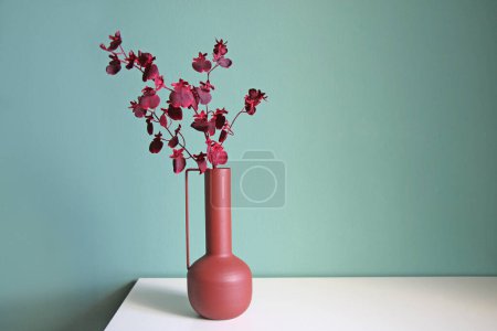 Blühender Zweig in einer modernen Keramikvase auf einem weißen Tisch. Platz für Ihren Text.