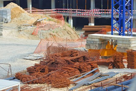 Stapel rostiger Bewehrungen auf einer Baustelle mit Baumaterialien und Barrieren