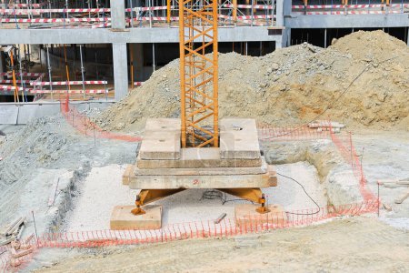 Detailed view of a crane's foundation and dugup earth at an active building site, with safety barriers