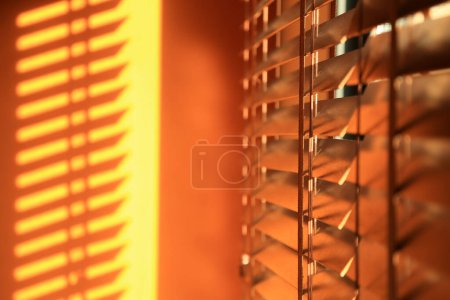 Téléchargez les photos : Fond orange abstrait. Stores en bois illuminés par le soleil couchant au foyer flou. Lumière du coucher du soleil qui traverse les stores de la fenêtre. - en image libre de droit