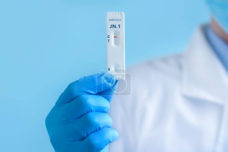 Téléchargez les photos : Un médecin portant un masque protecteur et des gants montre un test de laboratoire rapide pour la souche Covid-19 New Variant JN.1 pour détecter les anticorps IgM et IgG contre le nouveau coronavirus. Résultat négatif - en image libre de droit