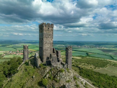Téléchargez les photos : Vue aérienne des vestiges du château médiéval de Hazmburk avec une tour circulaire et rectangulaire se trouvent au sommet de cet endroit de randonnée à faible pic avec vue panoramique. - en image libre de droit