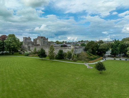 Téléchargez les photos : Vue aérienne du château et de la ville de Cahir en Irlande avec Tower House, château extérieur, tours circulaires, rectangulaires, salle de banquette, gardant la traversée sur la rivière Suir avec une cascade et un terrain de golf - en image libre de droit