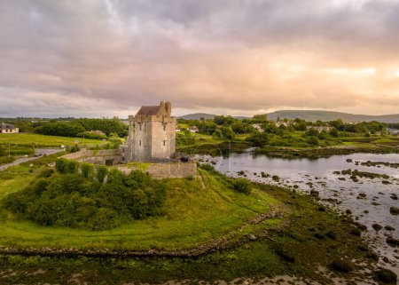 Foto de Vista aérea del castillo de Dunguaire es una casa torre del siglo XVI en la orilla sureste de la bahía de Galway en el condado de Galway, Irlanda, cerca de Kinvara con cielo atardecer dramático - Imagen libre de derechos