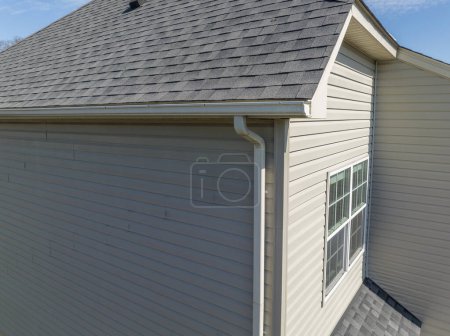 Photo for Aerial closeup view gable with vinyl siding, white frame gutter guard system, fascia, drip edge, soffit, on a pitched roof attic at a luxury American single family home neighborhood USA - Royalty Free Image