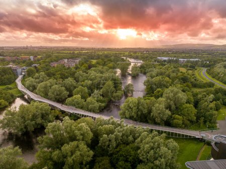 Aerial panoramic view of Living Bridge, curving modern pedestrian crossing over the Shannon river at the University of Limerick with stunning sunset