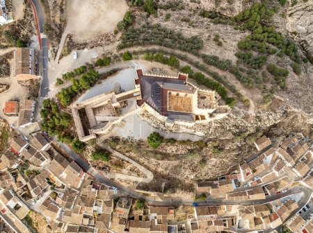 Vista aérea del castillo de Vélez Blanco en una colina y pueblo con una o dos casas de piso paredes encaladas y techos de azulejos con un cielo nublado dramático en Andalucía España
