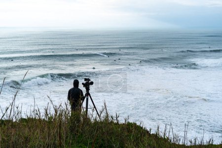 Photo for Rear view of videographer filming surfers in Nazare Surfing Challenge - Royalty Free Image
