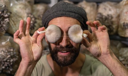 Portrait of young hispanic man holding oyster mushroom in front of his eyes. Crazy mushrooms farmer
