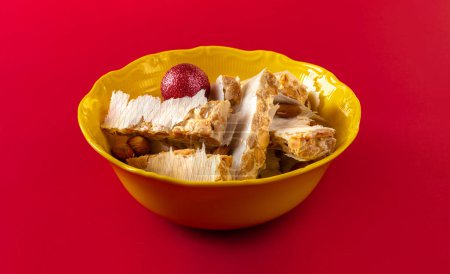 Photo for Almond Alicante turron dessert slices with Christmas boll in yellow plate on red background. traditional dessert in Spain. - Royalty Free Image