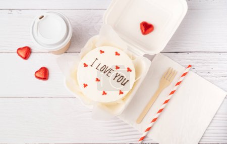 Bento cake with text I love you, on white wooden planks background. Korean style cakes in a box for one person and coffee cup. Flat lay