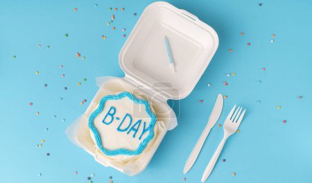 Flay mit Geburtstagstorte auf papierblauem Hintergrund mit Gabel und Messer. Kuchen im koreanischen Stil in einer Schachtel für eine Person