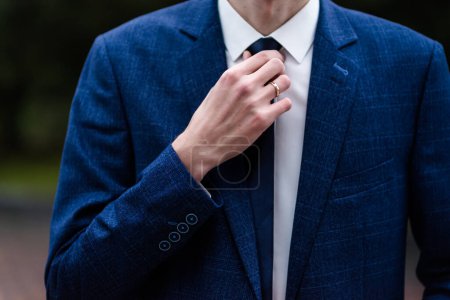 Photo for Elegant man tying his tie over black shirt. Adjusting tie. Black and violet. Young business man dressing, isolated on black background. Groom adjusting his tie. blue suit - Royalty Free Image
