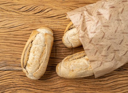 Téléchargez les photos : Pain français à grains entiers, pain salé ou pistolet sur un sac en papier sur une table en bois. - en image libre de droit