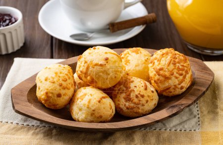 Téléchargez les photos : Petit pain au fromage brésilien typique dans une assiette avec café, confiture et jus d'orange sur une table en bois. - en image libre de droit