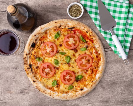 Foto de Pizza estilo margherita sobre mesa de madera con vino, orégano y espátula. - Imagen libre de derechos