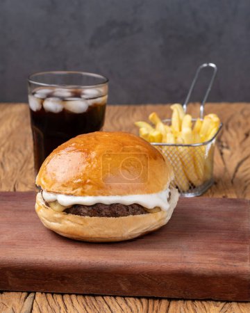 Photo for Cheeseburger with mayonnaise over wooden board with french fries and soda. - Royalty Free Image