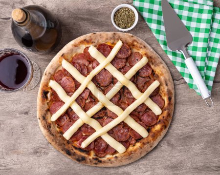 Calabrian sausage and Catupiry cream cheese style pizza over wooden table with wine, oregano and spatula.