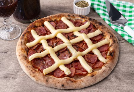 Calabrian sausage and Catupiry cream cheese style pizza over wooden table with wine, oregano and spatula.