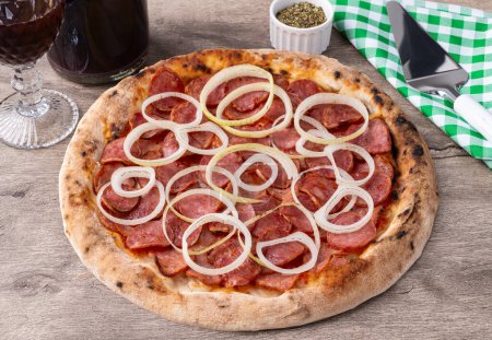 Wurst-Pizza aus Kalabrien über Holztisch mit Wein, Oregano und Spachtel.
