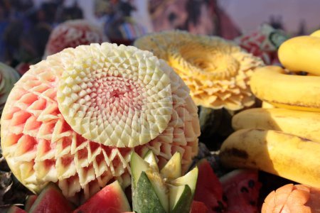 Téléchargez les photos : Fleurs sculptées de pastèque. Détail en gros plan de fruits thaïlandais sculptés dans une belle forme florale au-dessus d'une pastèque utilisée comme décoration dans un banquet extérieur. Fête conceptuelle. Mise au point sélective - en image libre de droit