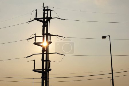 Foto de Silhouette of twin electric poles at sunset. View of electric tower with high voltage switch fuses in evening with sun on dim sky background with copy space and focus. - Imagen libre de derechos
