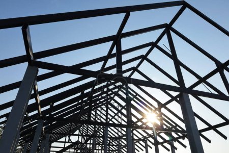 Silhouette of a metal roof structure. Structural steel beams roof of house or building on blue sky background with sunset in bottom view with copy space and focus.