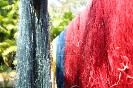 Photo for Silk threads hanging in the sunlight. Close-up of rows of silk threads dyed with natural dyes hanging on a bamboo rack to dry in the sunlight in Thailand with copy space with selective focus. - Royalty Free Image