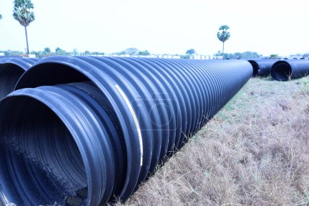 Plastic corrugated drainage pipe. Large black HDPE plastic pipe for sewage and water supply installation lies on the lawn at an outdoor construction site with copy space with selective focus.