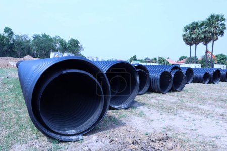 Plastic corrugated drainage pipe. Large black HDPE plastic pipe for sewage and water supply installation lies on the lawn at an outdoor construction site with copy space with selective focus.