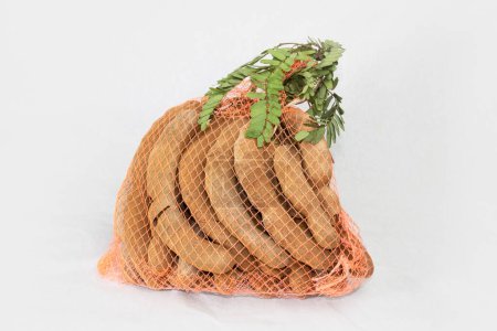 A sack of Pile of tamarind fruits with green leaves isolated on white background.
