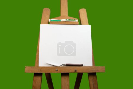 Foto de Un lienzo sobre caballete de pintura con cuchillo de paleta, espátula y color para pintar, materiales artísticos sobre fondo verde. - Imagen libre de derechos