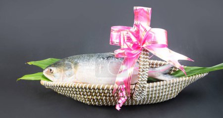 Un poisson Hilsha dans un boisseau artisanal en forme de bateau utilisé comme panier cadeau dans les occations festives telles que Jamai Shashthi, Pohela boishakh etc au Bangladesh et en Inde, décoré avec un ruban décoratif.