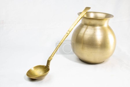 Empty golden brass vessels used as a water pot for traditional rituals during religious hindu festivals isolated in a white background. And a brass ghee or curry Spoon.