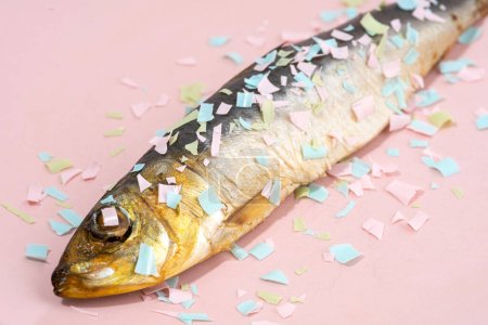 Fish covered microplastic on a pink plate. Impact of micro plastic on the food chain. The idea of microplastic pollution. Concept of environmental damage. Close-up image.
