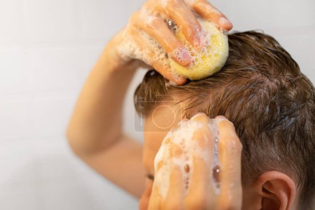 Un homme utilise un bar de shampooing solide dans la salle de bain. Soins capillaires durables. Un shampooing appliqué sur le cuir chevelu. Plastique libre, zéro déchet vivant, ingrédients à faible teneur en eau. Responsabilité de la nature.