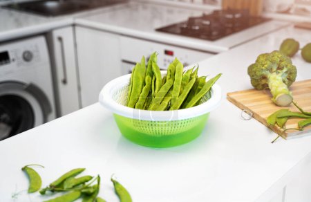 Photo for Modern kitchen interior with green vegetables, romano helda beans, green peas and broccoli on the table. Bright white kitchen. The concept of a healthy nutrition and vegetarian lifestyle. Copy space. - Royalty Free Image