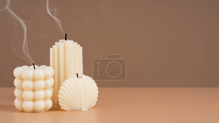 Photo for Handmade olive wax different forms candle with smoke from the wick on a brown beige background. Sustainability vegan candle, natural materials. Minimalistic, modern photo. Copy space. Banner - Royalty Free Image