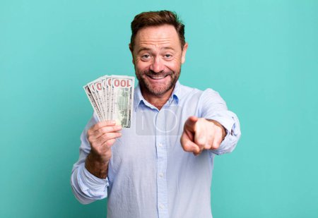 Téléchargez les photos : Middle age man pointing at camera choosing you. dollar banknotes concept - en image libre de droit