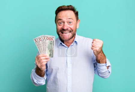 Téléchargez les photos : Middle age man feeling shocked,laughing and celebrating success. dollar banknotes concept - en image libre de droit