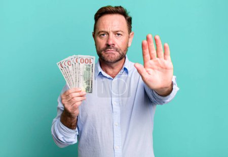 Téléchargez les photos : Middle age man looking serious showing open palm making stop gesture. dollar banknotes concept - en image libre de droit