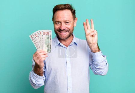 Photo for Middle age man smiling and looking friendly, showing number three. dollar banknotes concept - Royalty Free Image