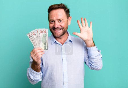 Photo for Middle age man smiling and looking friendly, showing number five. dollar banknotes concept - Royalty Free Image