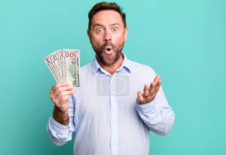 Téléchargez les photos : Middle age man amazed, shocked and astonished with an unbelievable surprise. dollar banknotes concept - en image libre de droit