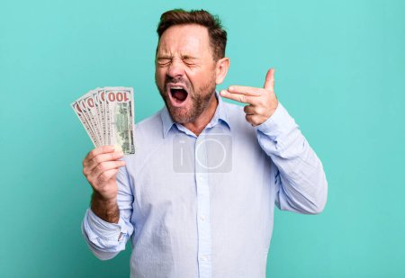 Photo for Middle age man looking unhappy and stressed, suicide gesture making gun sign. dollar banknotes concept - Royalty Free Image