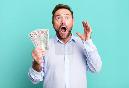 Photo for Middle age man screaming with hands up in the air. dollar banknotes concept - Royalty Free Image
